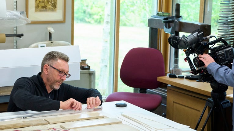 A cameraman filming a conservator working on Sackville family patents from Knole, Kent on a table for Hidden Treasures